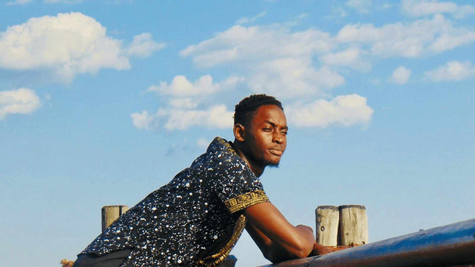 Yusuf Sanni leaning on a wooden railing beneath a blue sky.